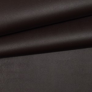May include: Close-up of a dark brown faux leather fabric. The fabric has a textured surface and is folded in half.
