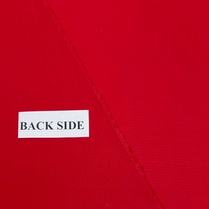 May include: A close-up of a red fabric with a textured surface. The fabric is folded in half and the back side is labeled with a white tag that says "BACK SIDE".