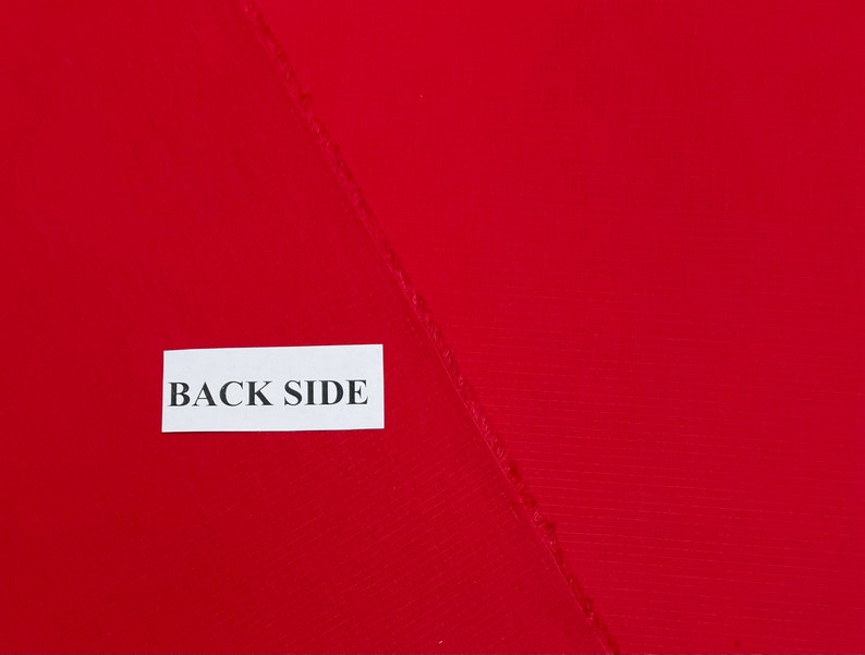 May include: A close-up of a red fabric with a textured surface. The fabric is folded in half and the back side is labeled with a white tag that says "BACK SIDE".