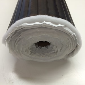 May include: A roll of black quilted upholstery fabric with white backing. The fabric is rolled up and secured with a white tape.