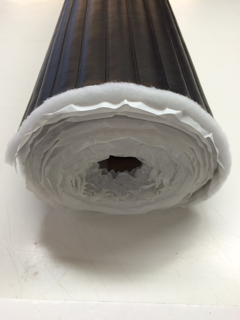 May include: A roll of black quilted upholstery fabric with white backing. The fabric is rolled up and secured with a white tape.