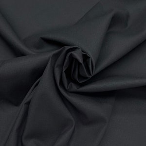 May include: Black fabric with a smooth, slightly textured surface. The fabric is folded and draped, creating a soft, flowing look.