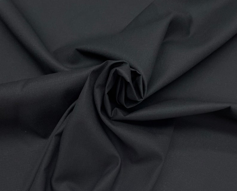 May include: Black fabric with a smooth, slightly textured surface. The fabric is folded and draped, creating a soft, flowing look.