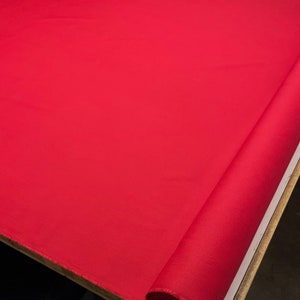 May include: A roll of bright red fabric. The fabric is smooth and has a slight sheen.