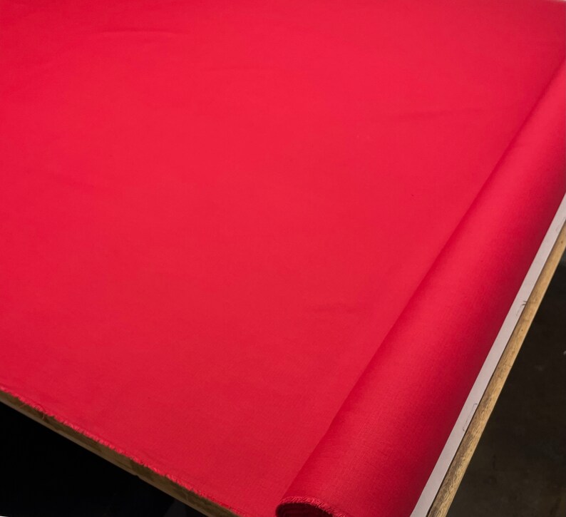 May include: A roll of bright red fabric. The fabric is smooth and has a slight sheen.