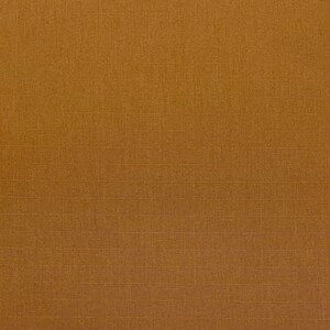 May include: A close-up of a textured, golden-brown fabric. The fabric has a subtle grid pattern created by fine, horizontal and vertical lines. The overall appearance is a solid, warm colour with a slightly rough texture.