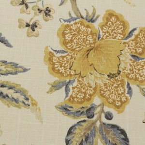 May include: Close-up of a floral fabric featuring large, yellow and brown flowers with intricate details. The flowers are set against a cream-colored background with subtle texture. The design includes gray and brown leaves and stems, creating a natural, botanical theme.