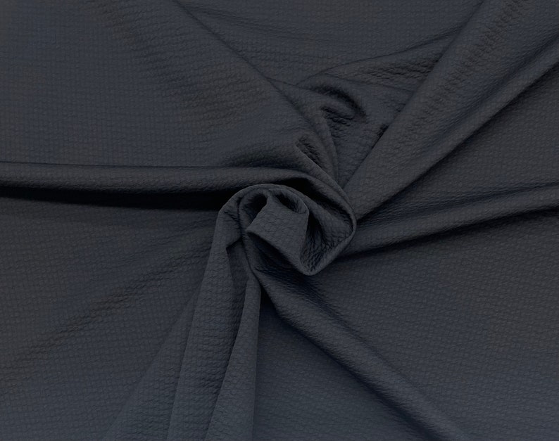 May include: A close-up of a dark gray textured fabric with a waffle-like pattern. The fabric is folded and draped, showing its soft and pliable texture.