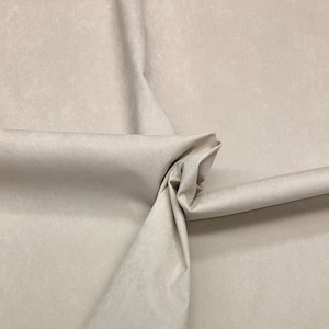 May include: Close-up of a light beige fabric with a soft, textured surface. The fabric is folded and draped, showcasing its smooth texture.