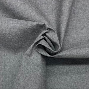 May include: A close-up shot of gray fabric with a textured appearance. The fabric is swirled and folded, creating shadows and depth. The material has a subtle, woven pattern, and the overall tone is a neutral gray.
