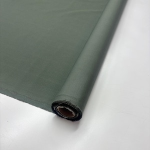 May include: A roll of olive green fabric. The fabric is tightly rolled, revealing a textured surface and a raw edge. The color is a muted, earthy tone, suitable for various sewing and crafting projects.