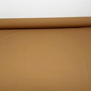 May include: A roll of tan fabric, unrolled on a white surface. The fabric is a solid colour and appears to be smooth. The roll is cylindrical and positioned at the top of the image.