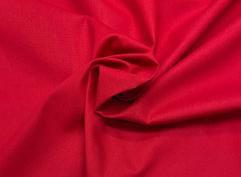 May include: A close-up of a red fabric with a smooth, textured surface. The fabric is folded and draped, creating a soft, flowing look.