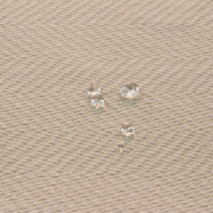 May include: Three clear glass beads on a beige textured fabric surface.