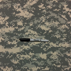May include: A close-up of a digital camouflage fabric with a black Sharpie fine point marker on top of it.