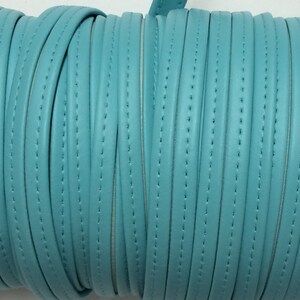 May include: A spool of teal blue faux leather cord with a stitched edge. The cord is wound tightly around the spool.
