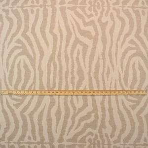 May include: Beige fabric with a white zebra print pattern. A wooden ruler is placed on top of the fabric for scale.