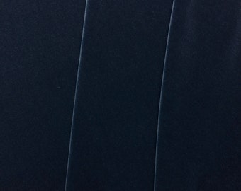 May include: A close-up of a dark blue fabric with a smooth, velvety texture. The fabric is folded in thirds, creating three vertical panels.