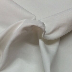 Puede incluir: Tela blanca de canal&eacute; con una textura suave. La tela est&aacute; doblada y drapeada, mostrando su naturaleza suave y flexible.