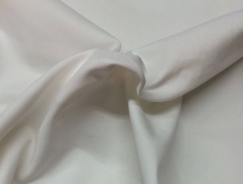 Puede incluir: Tela blanca de canal&eacute; con una textura suave. La tela est&aacute; doblada y drapeada, mostrando su naturaleza suave y flexible.