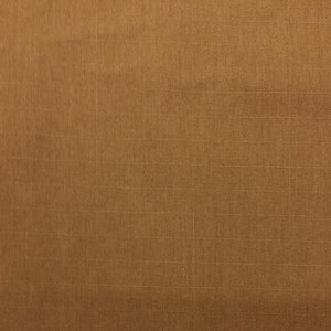 May include: Close-up of a textured, golden-brown fabric. The material has a subtle sheen and a grid-like pattern created by the weave. The color is a warm, earthy tone.