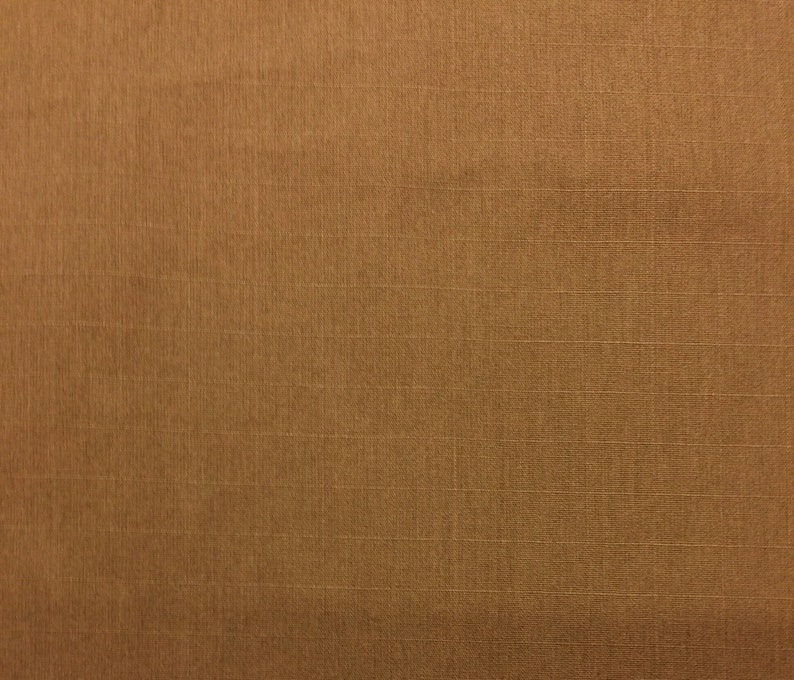 May include: Close-up of a textured, golden-brown fabric. The material has a subtle sheen and a grid-like pattern created by the weave. The colour is a warm, earthy tone.