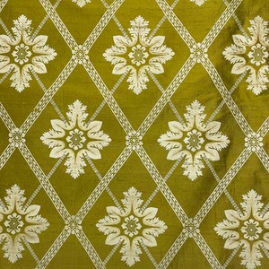 May include: A green fabric with a white repeating pattern of stylized flowers and diamond shapes.