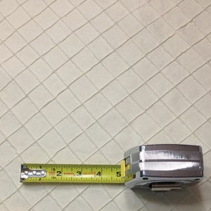 May include: A yellow measuring tape with a silver case. The tape is extended to 12.7 cm and shows the numbers 1, 2, 3, 4, and 5. The tape is on a white textured surface.