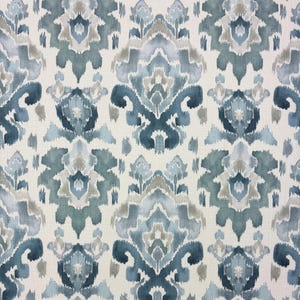 May include: A textile fabric featuring a repeating damask-inspired pattern in shades of teal, slate blue, and soft gray against an off-white background. The design displays blurred, watercolor-like edges characteristic of an ikat print style.