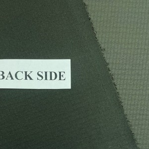 May include: Close-up of two fabric swatches in shades of green. The left swatch is a solid, darker green, while the right swatch is a lighter green with a textured, grid-like pattern. A white label with the text "BACK SIDE" is visible.