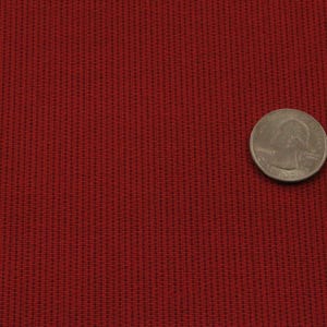 May include: Close-up of a red fabric with a textured weave. A US quarter is placed on the fabric for scale.