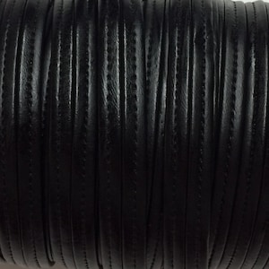 Puede incluir: Un carrete de cordón de cuero negro con una superficie texturizada. El cordón está enrollado firmemente alrededor del carrete.