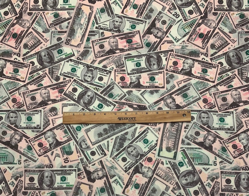 Pode incluir: Um close-up de um tecido com um padr&atilde;o de notas de d&oacute;lar americano em v&aacute;rias denomina&ccedil;&otilde;es. As notas s&atilde;o impressas em tons de verde, preto e branco, e est&atilde;o dispostas em um padr&atilde;o aleat&oacute;rio. Uma r&eacute;gua de madeira &eacute; colocada sobre o tecido, com o texto "WESTCOTT" vis&iacute;vel.