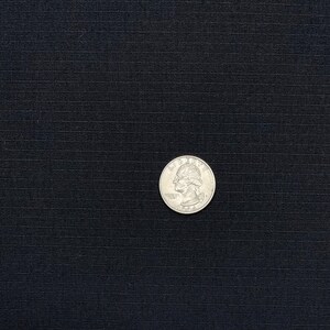 May include: A close-up of a black fabric with a subtle texture. A silver US quarter is placed on the fabric.