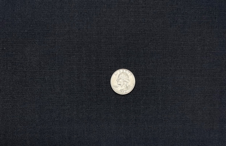 May include: A close-up of a black fabric with a subtle texture. A silver US quarter is placed on the fabric.