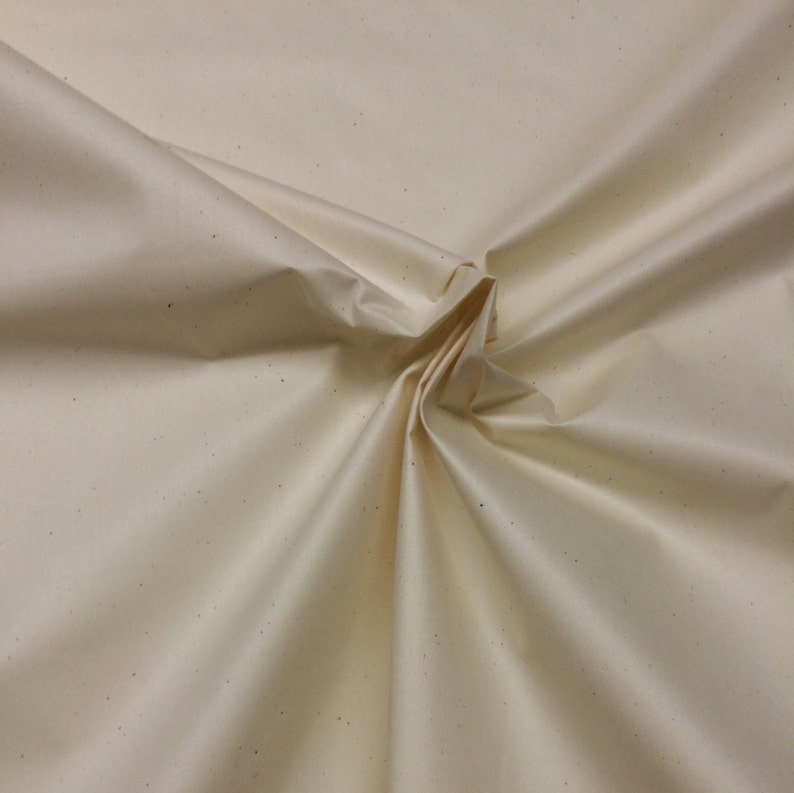 May include: A close-up of a cream-coloured fabric with a subtle speckled texture. The fabric is folded and draped, showcasing its soft and smooth surface.