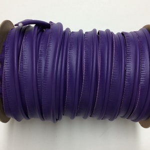 May include: A spool of purple faux leather trim with a textured edge. The trim is wound around a cardboard core.