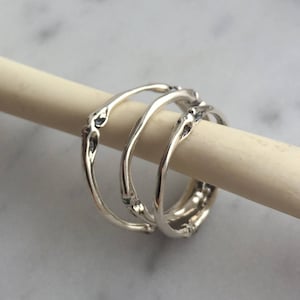 May include: Three silver rings with a textured, organic design. The rings are stacked on top of each other.