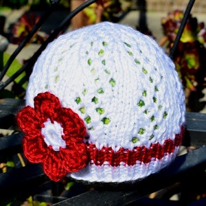 May include: White crocheted hat with a red flower and a red stripe around the bottom.
