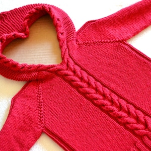 May include: Red knitted sweater with a heart-shaped hood and a cable knit pattern.
