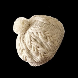 May include: A white knitted beanie with a pom pom on top. The beanie has a cable knit pattern.