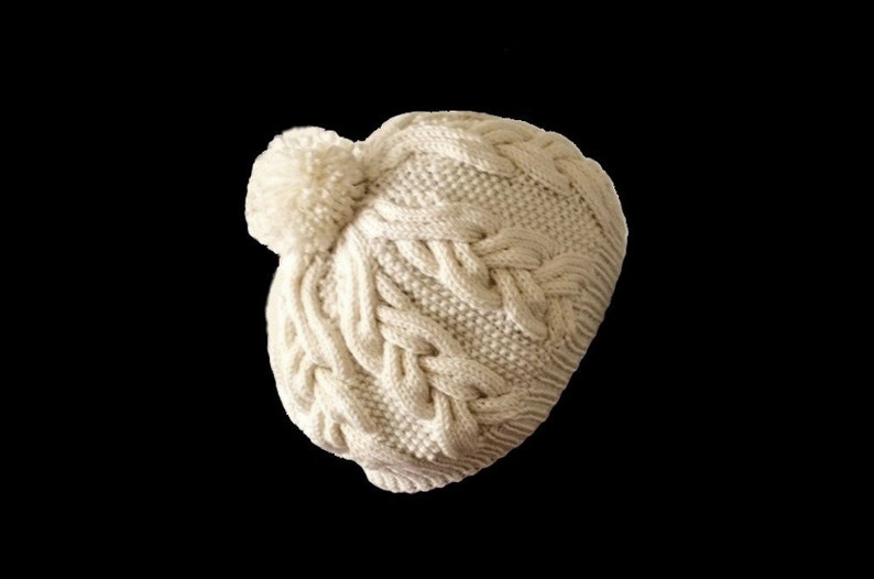 May include: A white knitted beanie with a pom pom on top. The beanie has a cable knit pattern.