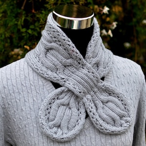 May include: A gray knitted scarf with a unique, intricate design. The scarf is made of soft yarn and has a comfortable feel.