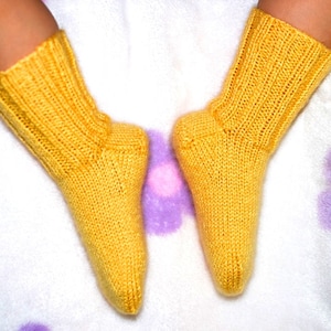 May include: A pair of yellow knitted baby socks on a white background with purple flowers.