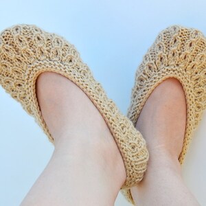 May include: A pair of beige knitted slipper socks with a delicate pattern. The socks are worn on a person's feet.
