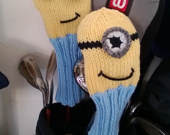 May include: Two knitted golf club head covers shaped like the Minions from the Despicable Me movies. The covers are blue and yellow with black eyes and a black mouth. The covers are in a golf bag with golf clubs.