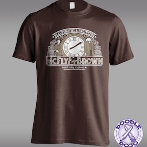 May include: Brown t-shirt with a vintage-style graphic of two figures standing in front of a clock with the text "Blacksmiths & Engineers McFly & Brown Hill Valley, California".