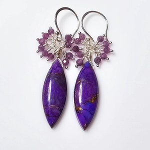 May include: Purple gemstone earrings with a silver wire wrapped design and small purple beads. The earrings are dangle style and feature a teardrop shaped gemstone.
