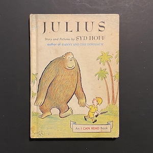 Puede incluir: Libro infantil vintage "JULIUS" de Syd Hoff. La portada presenta una criatura peluda y amigable tomados de la mano con un niño pequeño. El título y el autor son prominentes, con el texto "An I CAN READ Book".