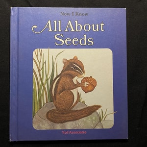 May include: A blue book titled "Now I Know All About Seeds" with a picture of a brown and white squirrel holding an acorn on the cover. The book is published by Troll Associates.